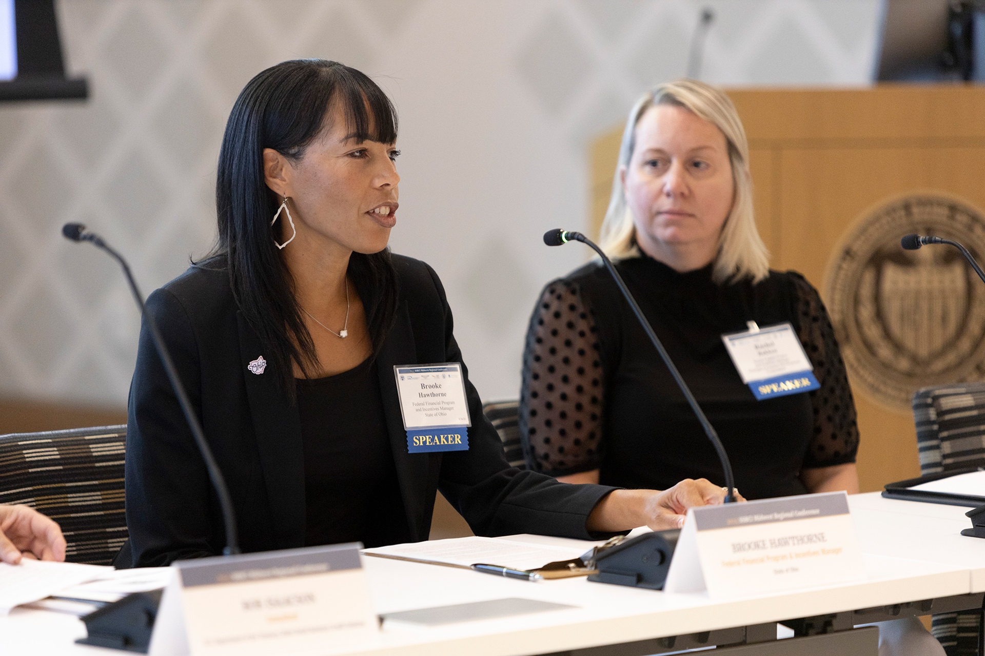 A person speaking into the microphone, while another panelists looks on.