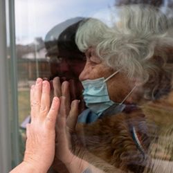Senior woman places palm against glass