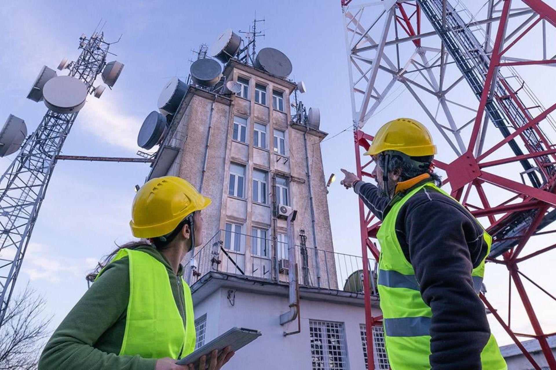 Workers in hard hats evaluate broadband tower