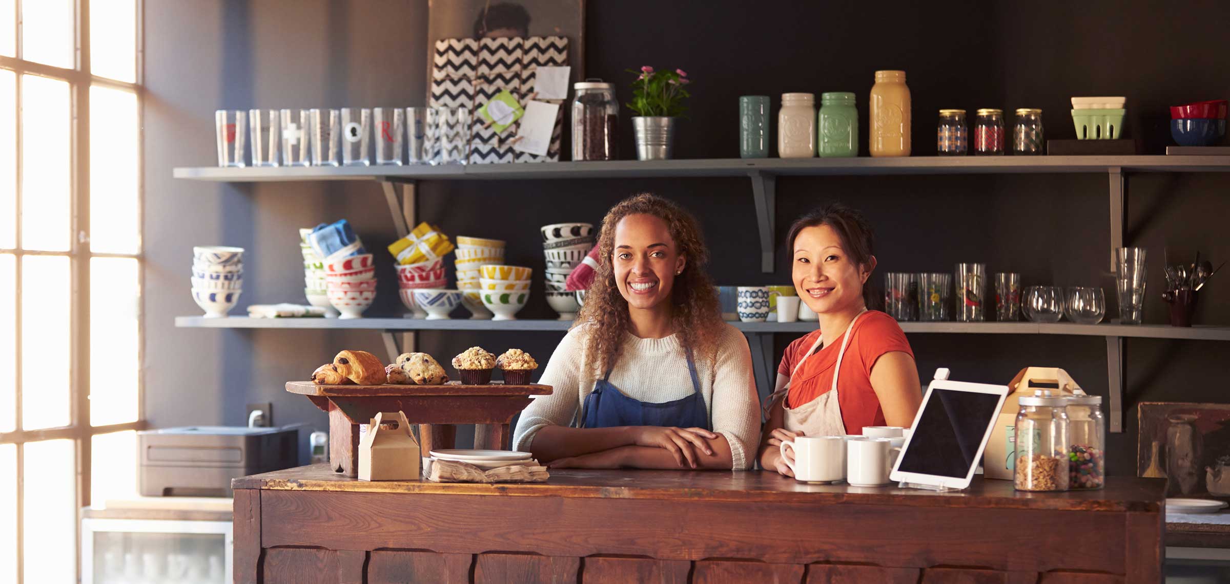 Two women stand behind a wooden coffee shop counter