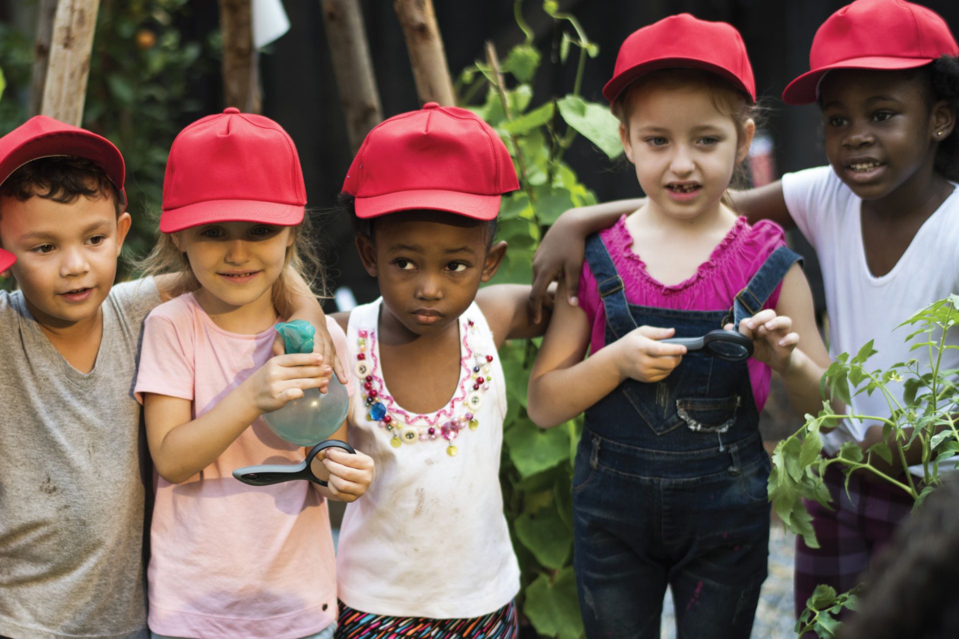 Group of five children wearing red hats holding magnifying glasses