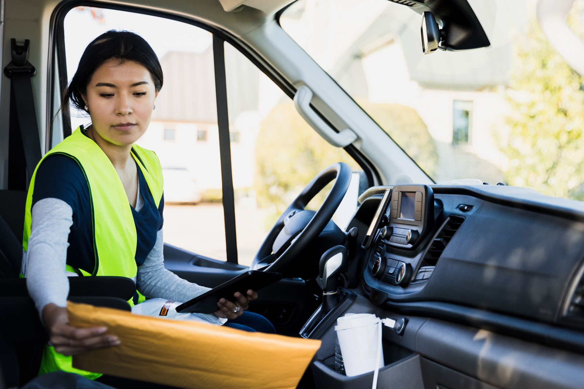 Delivery person sits inside their truck looking at a yellow envelope