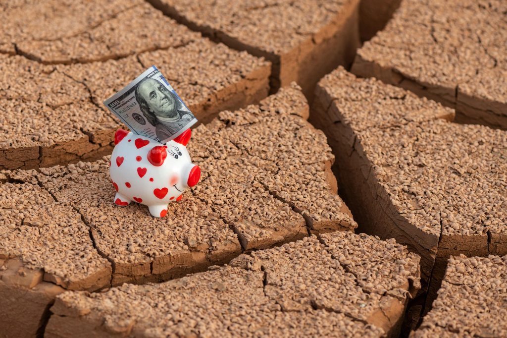 White and red polka dot piggy bank with cash standing on cracked desert