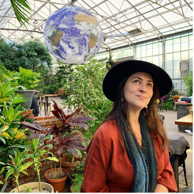 Ashley Putnam in a green house look up towards a globe with a smile on her face.