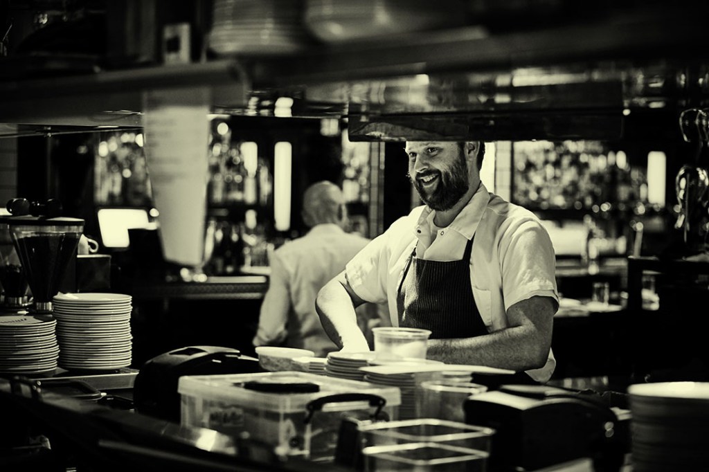 A person wearing an apron standing behind a counter.