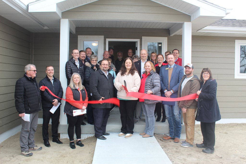 A group of people at a ribbon cutting ceremony in front of a new home.