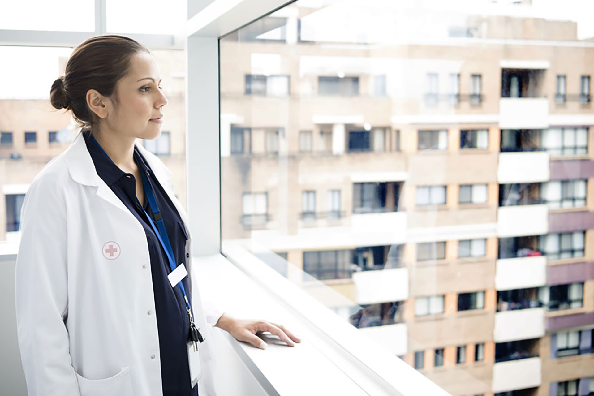 A medical practitioner looking out a window of health care facility in urban environment.