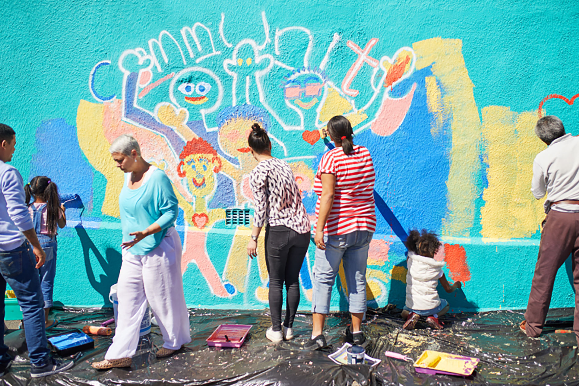 A group of people painting a community mural on the side of a building.