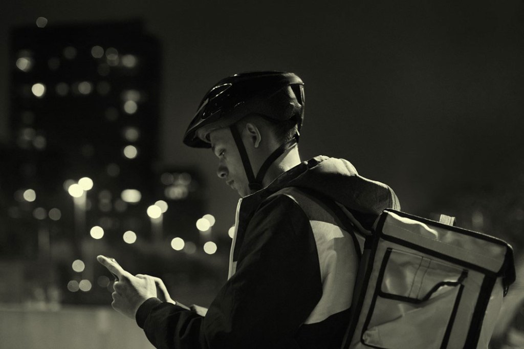 Delivery rider at dusk looking at the smartphone.