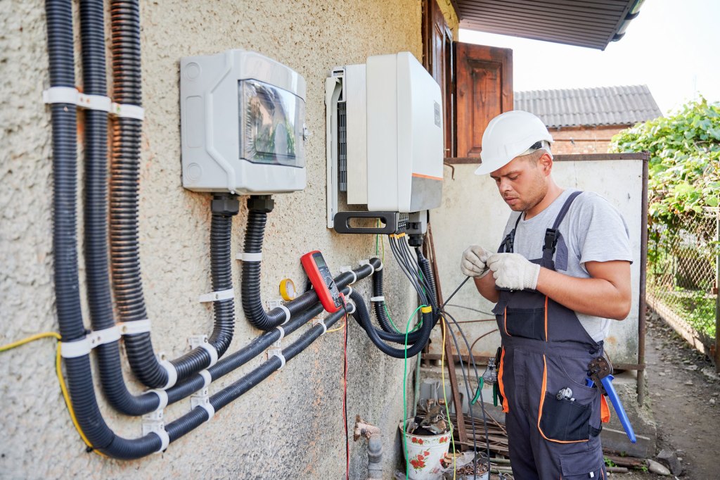 Electrician installing solar panel system, wiring inverter and electric box.