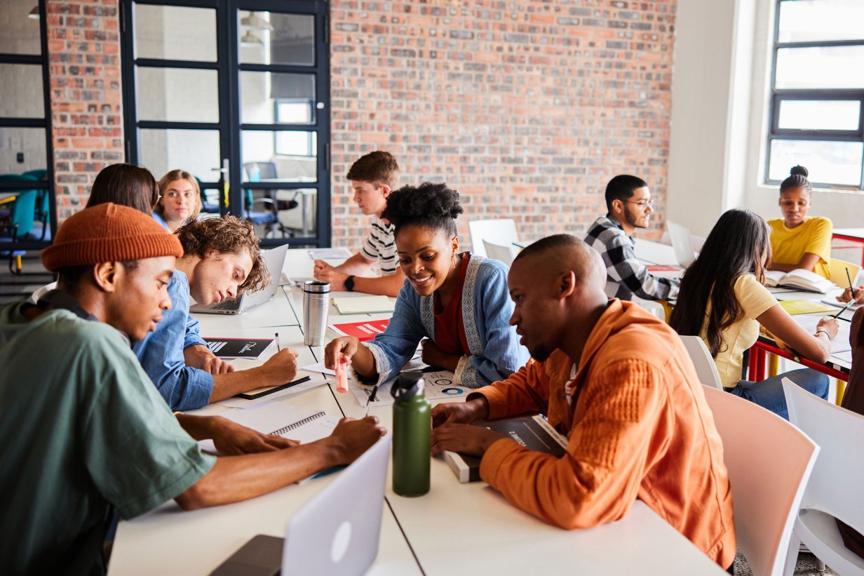 Group of diverse students studying together while sitting around a table between classes at school.