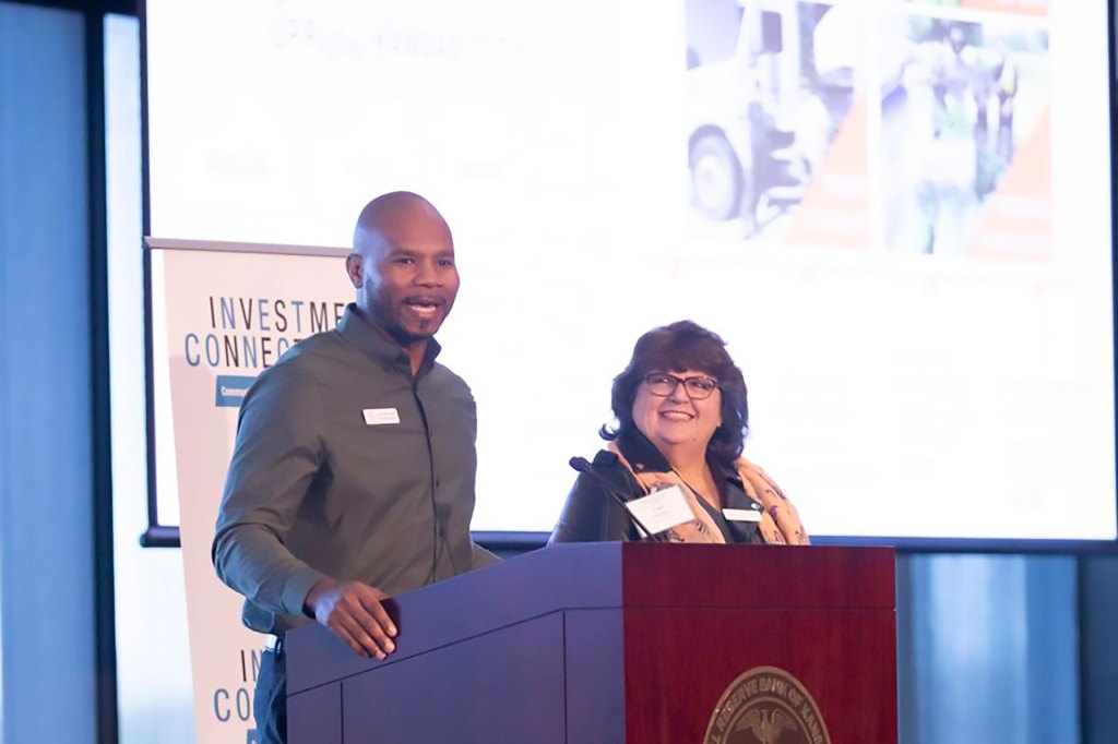 Two people smiling and standing at a podium addressing an audience at a recent Kansas City Fed Investment Connection event.