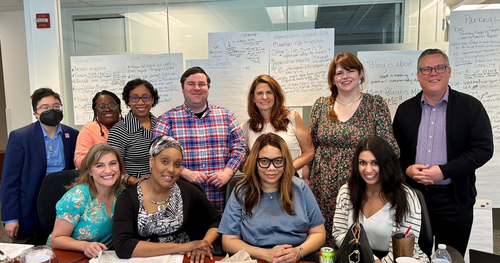 A group photo of NDI meeting participants gathered together in a meeting room surrounded by brainstorm ideas.