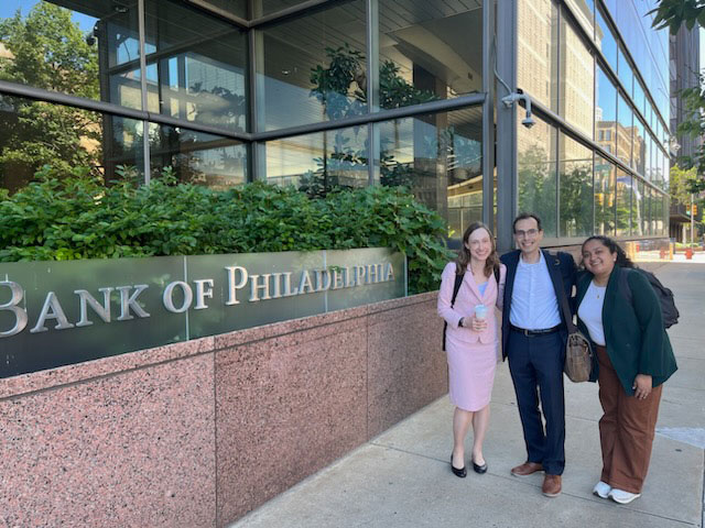 Three people pose together outside the Federal Reserve Bank of Philadelpha