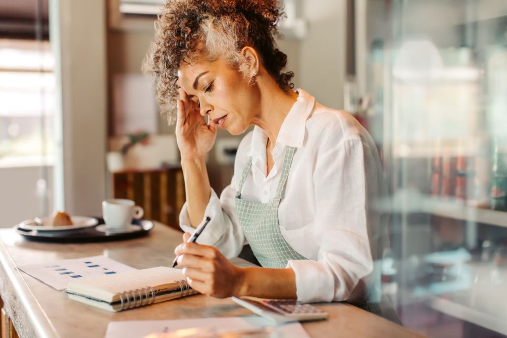 Female small business owner looking over notebook with a pen in her left hand.