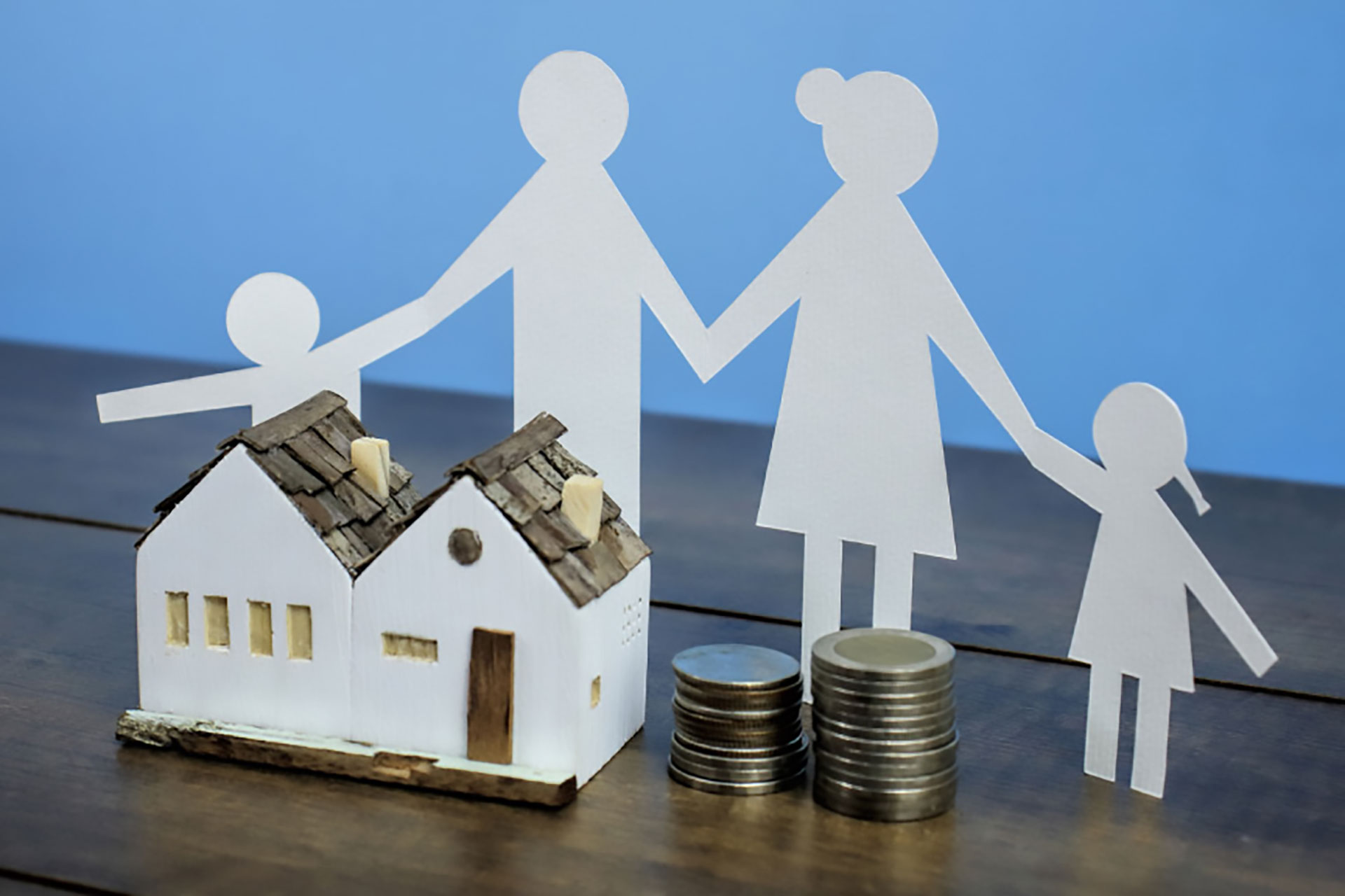 A paper cut-out of a family standing behind a small model home, and coins.