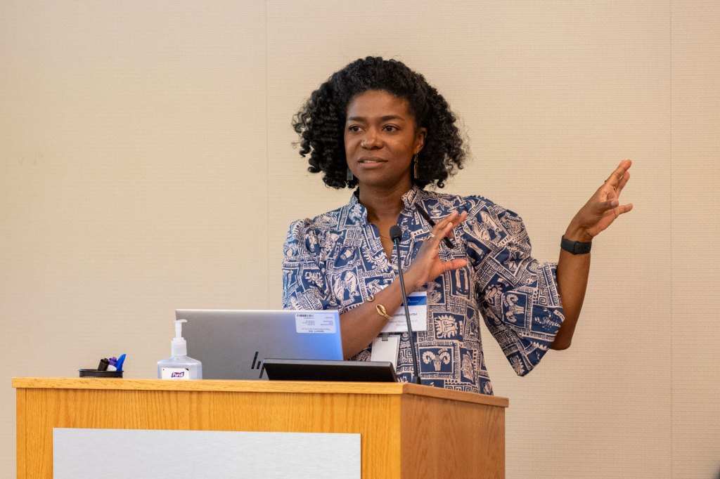 Woman standing at a podium using her hands to communicate a point.