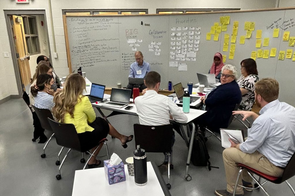 A small group discussion in front of a white board full of ideas for a vision and priorities.