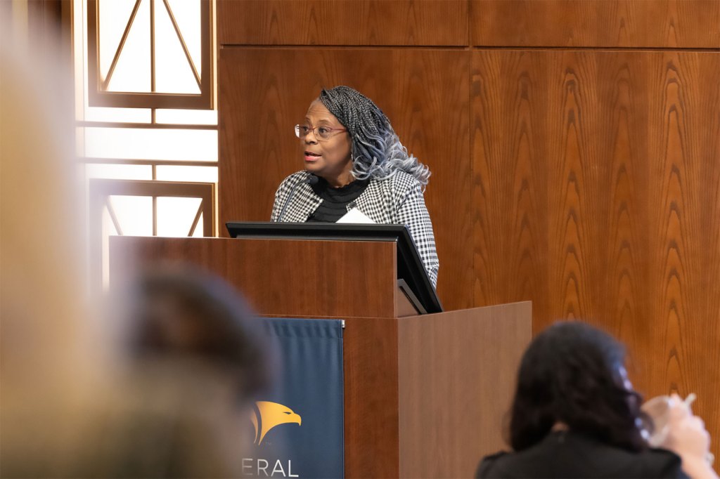 Constance Alberts stands behind a podium speaking to an audience at a recent Financial Inclusion Conference hosted by the St. Louis Fed.