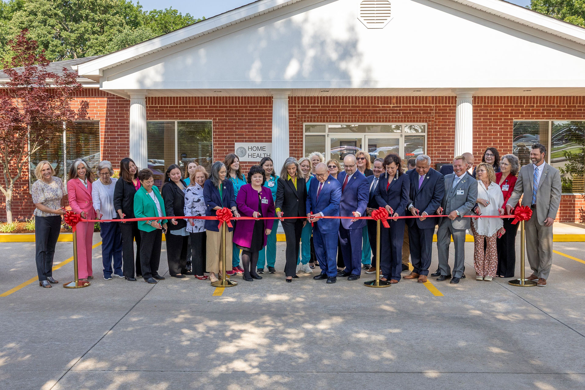 A group of people outside a new health center cutting a red ribbon.