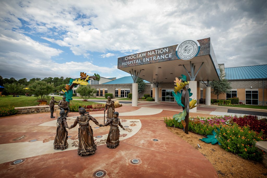 An entrance to a hospital. In front of the enterance is a series of monuments celebrating the Choctaw Nation