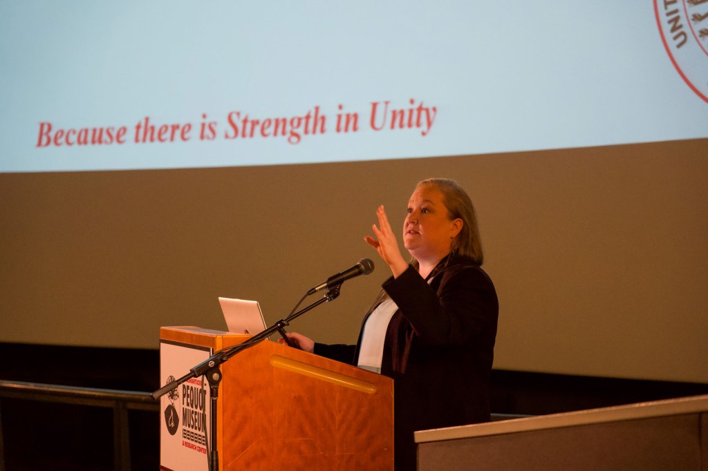 A woman stands behind a podium addressing an audience.