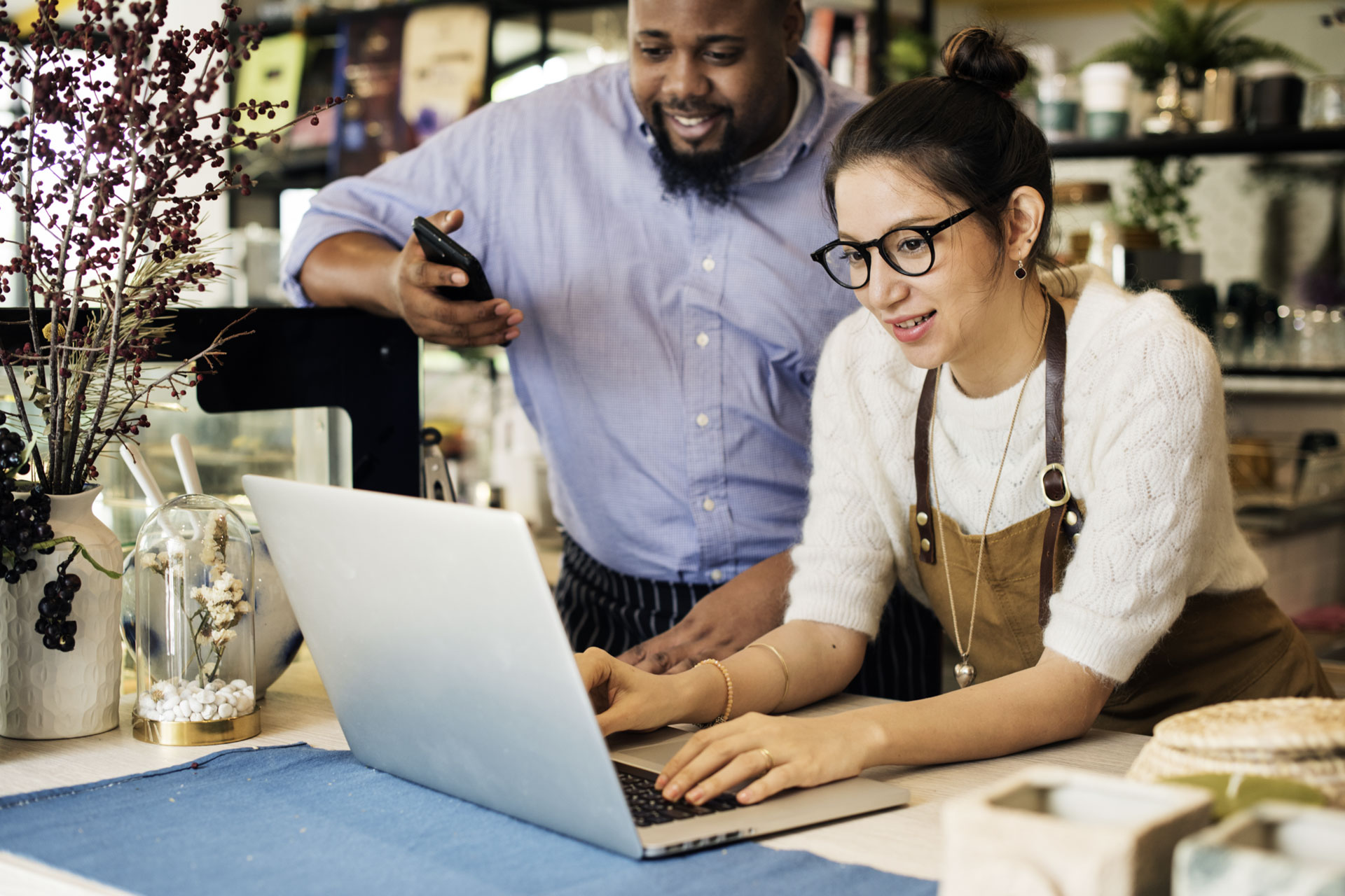Small business owner shows employee something on her laptop inside their retail store.