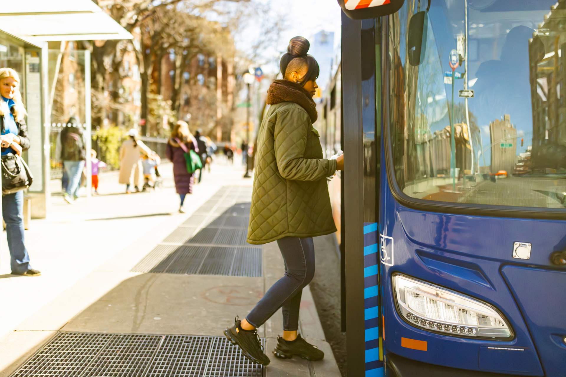 A person boarding a bus during a bright morning in the city.