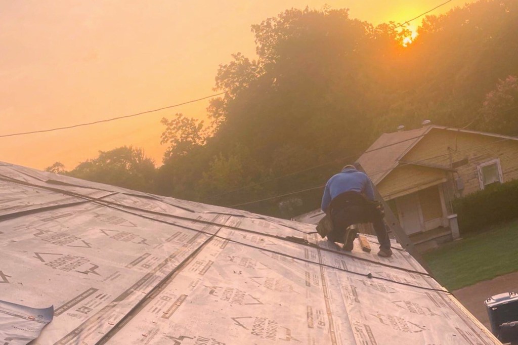 A roofer installs new shingles at sunrise on a home.