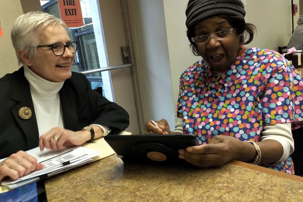 A technology coach helps an older woman new to using a tablet with help on how to use the tool.