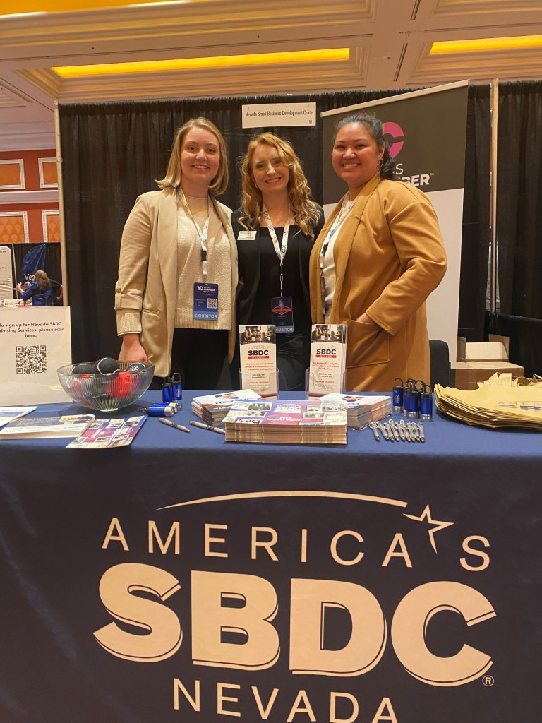Three women stand behind a tradeshow booth sharing resources on the Nevada Small Business Development Center.