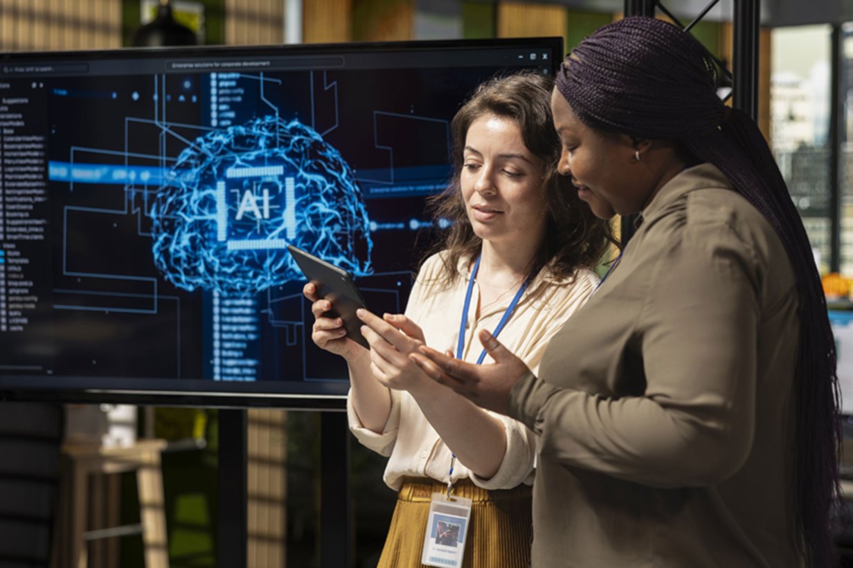 Two femails look up something on their phone next to a screen showing a brain with the word AI shown and a series of prompts in the background.