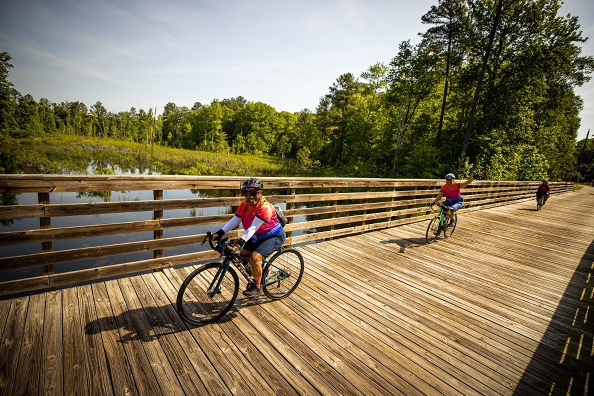 Cyclists riding along a wooden boardwalk section of the Virginia Capital Trail, a fully paved, 51.7-mile multi-use path connecting Richmond to Jamestown, Virginia.